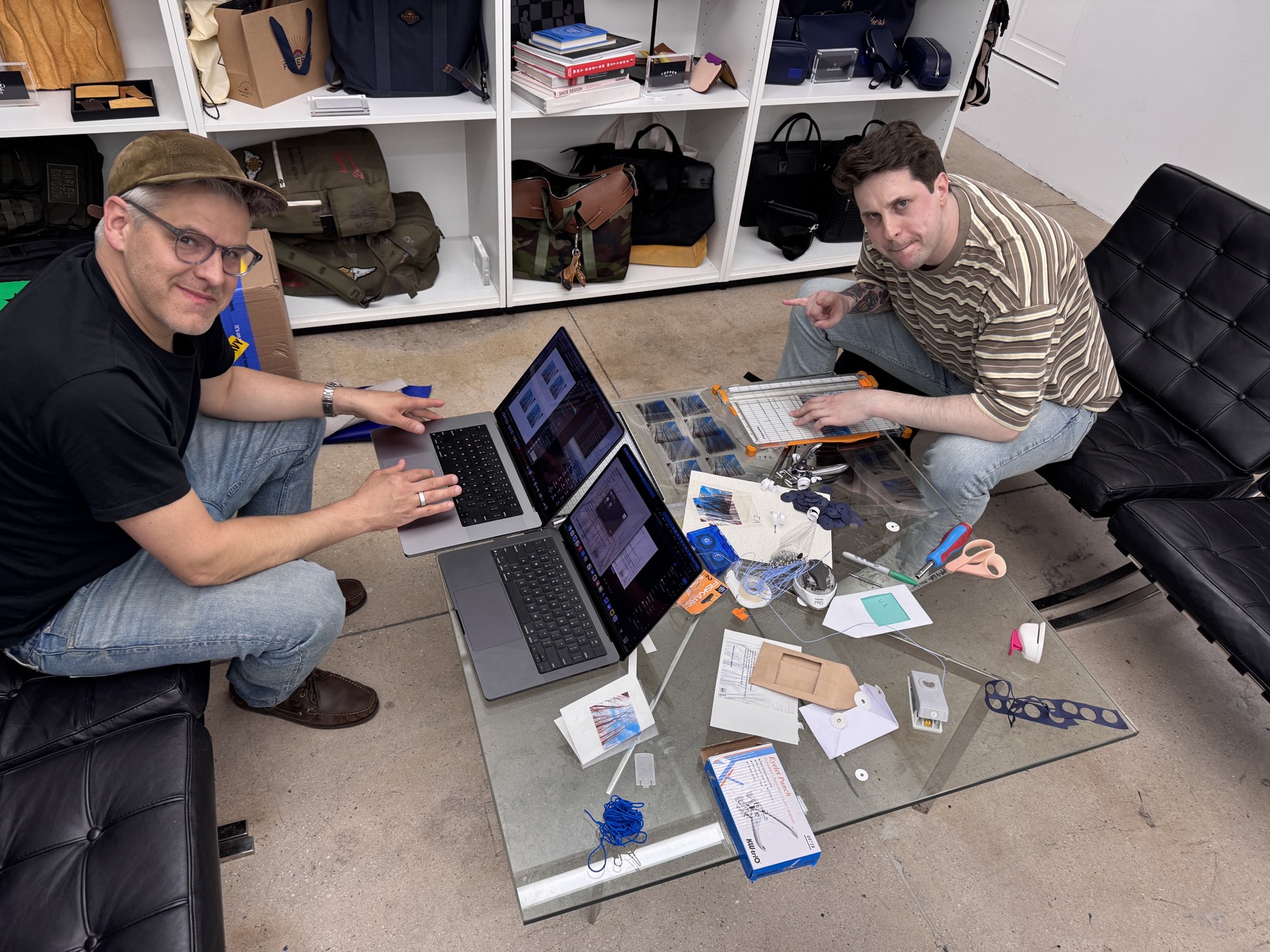 two people seated at a glass table assembling the cassettes, laptops and materials spread out